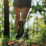 Kobieta biegnąca po leśnej ścieżce w sportowych butach i krótkich spodenkach