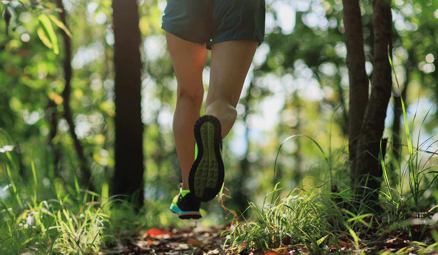 Kobieta biegnąca po leśnej ścieżce w sportowych butach i krótkich spodenkach